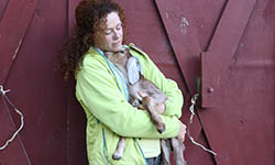 Cokie Berenyi cuddles a goat in front of a red barn door